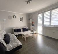 Wohnzimmer in einer Zweizimmerwohnung mit Sofas und einem Tisch, Licht scheint durch die Jalousien.