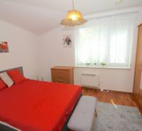 Ein Schlafzimmer in einem Einfamilienhaus mit roter Bettwäsche, einer Kommode und einem großen Fenster.