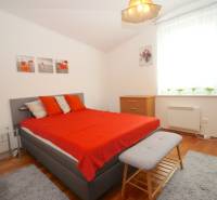 Schlafzimmer im Einfamilienhaus mit grauem Bett, roten Decken und Holzmöbeln.