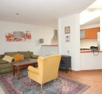 Wohnzimmer mit Teppich, grünem Sofa, gelbem Sessel und Küchenzeile in einem Einfamilienhaus.