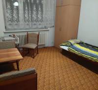 Ein Zimmer eines Einfamilienhauses mit Bett, Schrank, Tisch und Stühlen, in warmen Farben gehalten.