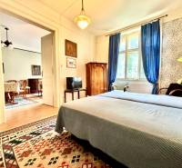 Schlafzimmer in einer 2-Zimmer-Wohnung mit Bett, blauen Vorhängen und orientalischem Teppich.