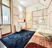 Badezimmer in einer 2-Zimmer-Wohnung mit Fenster, Badewanne und blauem Teppich.
