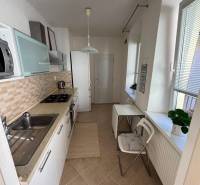 Küche in einer 2-Zimmer-Wohnung mit weißen Schränken und Fenstern mit Rollläden.