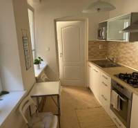 Küche in einer 2-Zimmer-Wohnung mit hellen Möbeln, Geräten und Esstisch.
