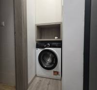 Waschmaschine in einem engen Raum einer Zweizimmerwohnung mit Holzverkleidung und Stauraum.