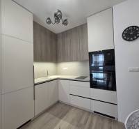 Küche in einer 2-Zimmer-Wohnung mit weißen und hölzernen Schränken, eingebauten Geräten, Uhr.