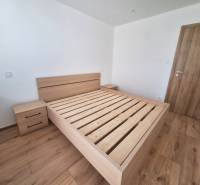 Schlafzimmer mit einem Holzbett in einer 2-Zimmer-Wohnung, ohne Matratze und mit einem Nachttisch.