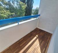 Balkon mit Holzboden und Blick auf Bäume in einer 2-Zimmer-Wohnung.