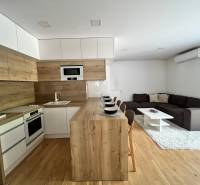 Küche verbunden mit Wohnzimmer in einer 3-Zimmer-Wohnung, mit Holzelementen und Sitzgelegenheit.
