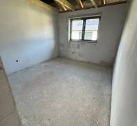 Unvollendeter Raum in einem Einfamilienhaus mit Fenster und freiliegenden Dachbalken.