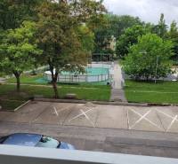 Blick aus einer 3-Zimmer-Wohnung in Bratislava - Ružinov auf der Mesačná-Straße, Parkplatz, Bäume und Spielplatz.