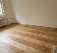 Ein leerer Raum in einer 3-Zimmer-Wohnung mit Parkettboden und einem Fenster.