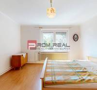 Ein Schlafzimmer in einem Einfamilienhaus mit einem Bett, einer Holzkredenz und einem Fenster mit Aussicht.