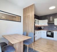 Die Küche in einer 4-Zimmer-Wohnung mit einem Ess-Set aus Holz und weißen Schränken.