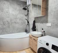 Badezimmer in einer 4-Zimmer-Wohnung mit Eckbadewanne und Waschmaschine.