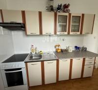 Küche in einer 2-Zimmer-Wohnung mit weißen Schränken und einem Herd mit Dunstabzugshaube.