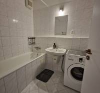 Badezimmer mit Badewanne und Waschmaschine in einer 2-Zimmer-Wohnung, Fliesenboden und weiße Fliesen.