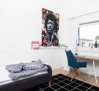 Einfaches Zimmer mit Tisch, Stuhl, Bett und einem bunten Bild an der Wand in einer 3-Zimmer-Wohnung.