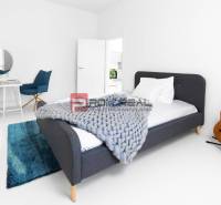 Einfaches Schlafzimmer mit Bett, Tisch, Stuhl und Gitarre in einer 3-Zimmer-Wohnung.
