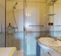 Badezimmer in einer 3-Zimmer-Wohnung, Duschkabine, Waschbecken, Spiegel und Regale.