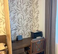 Ein Arbeitsbereich in einer 2-Zimmer-Wohnung mit einer Tapete mit Blattmuster und dunklen Möbeln.