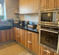 Küche mit Holzschränken, eingebautem Ofen und Fenster in einer Zweizimmerwohnung.