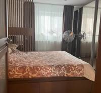 Schlafzimmer in einer Zweizimmerwohnung mit Doppelbett, Lampe und Fenstern mit schweren Vorhängen.