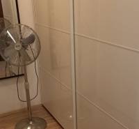 Ein Kleiderschrank in einer 2-Zimmer-Wohnung mit weißen Schiebetüren und einem Standventilator.