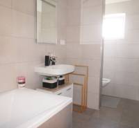 Badezimmer in einem Einfamilienhaus mit Badewanne, Waschbecken, Duschkabine und großformatigen Fliesen.