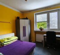 Ein Zimmer in einem Einfamilienhaus mit einem Bett, einem Schrank, einem Schreibtisch und gelben Wänden.