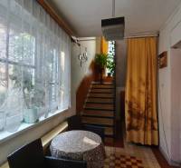 Ein Flur in einem Einfamilienhaus mit einem Fenster, Vorhängen, einem Tisch, Stühlen und Treppen mit Pflanzen.