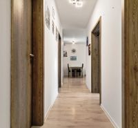 Ein Flur mit Holztüren, hellem Boden, Bildern an den Wänden neben einer 3-Zimmer-Wohnung.