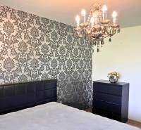 Schlafzimmer mit Kronleuchter und Tapetenwand in einem Einfamilienhaus. Boden mit Holzdekor.