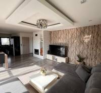 Wohnzimmer in einem Einfamilienhaus mit Sofa, Fernseher und Kamin, Boden mit Holzdekor.