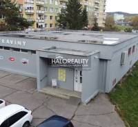 Ein Geschäftsgebäude in Rimavská Sobota, umgeben von Plattenbauten und geparkten Autos.