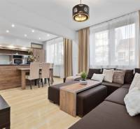 Wohnzimmer mit Holzboden in einer Zweizimmerwohnung mit Ecksofa und Küche.