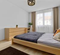 Schlafzimmer mit Bett und Kommode in einer 2-Zimmer-Wohnung, Boden mit Holzdekor.