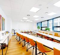 Ein Büro mit weißen Tischen, orangefarbenen Stühlen und einem Boden in Holzoptik.