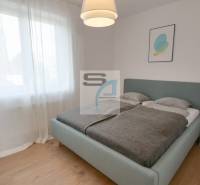 Schlafzimmer mit großem Bett, Vorhängen und Holzboden in einer Zweizimmerwohnung.