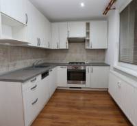 Küche in einer 3-Zimmer-Wohnung mit weißen Schränken und einem Boden in Holzoptik.