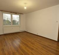 Ein Zimmer mit einem Holzboden in einer 3-Zimmer-Wohnung, weiße Wände, Fenster, Heizkörper.