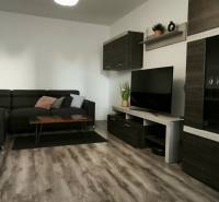Wohnzimmer mit dunklem Sofa, Fernseher und Holzboden in einer 3-Zimmer-Wohnung.