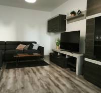 Wohnzimmer in einer 3-Zimmer-Wohnung mit dunklem Sofa und Boden in Holzoptik.