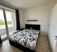 Schlafzimmer in einer 2-Zimmer-Wohnung mit Bett, Schrank und Balkon mit Holzboden.