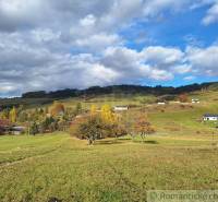Herbst in Liptovské Beharovce mit verstreuten Einfamilienhäusern auf grünen Hügeln unter einem bewölkten Himmel.