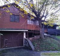 Eine Holzhütte in Dudince, umgeben von Bäumen und einem grasbewachsenen Hang.