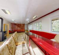 Ein Zimmer in einer Hütte mit Kachelöfen, Sofas, Holztischen und Blick auf den Wald.