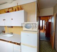 Küche in einer 3-Zimmer-Wohnung mit weißen Schränken und einem Kühlschrank auf einem Boden mit Holzdekor.