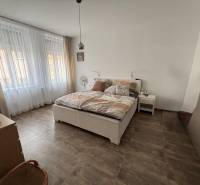 Schlafzimmer in einer 2-Zimmer-Wohnung mit großen Fenstern, einem Bett und einem Boden mit Holzdekor.